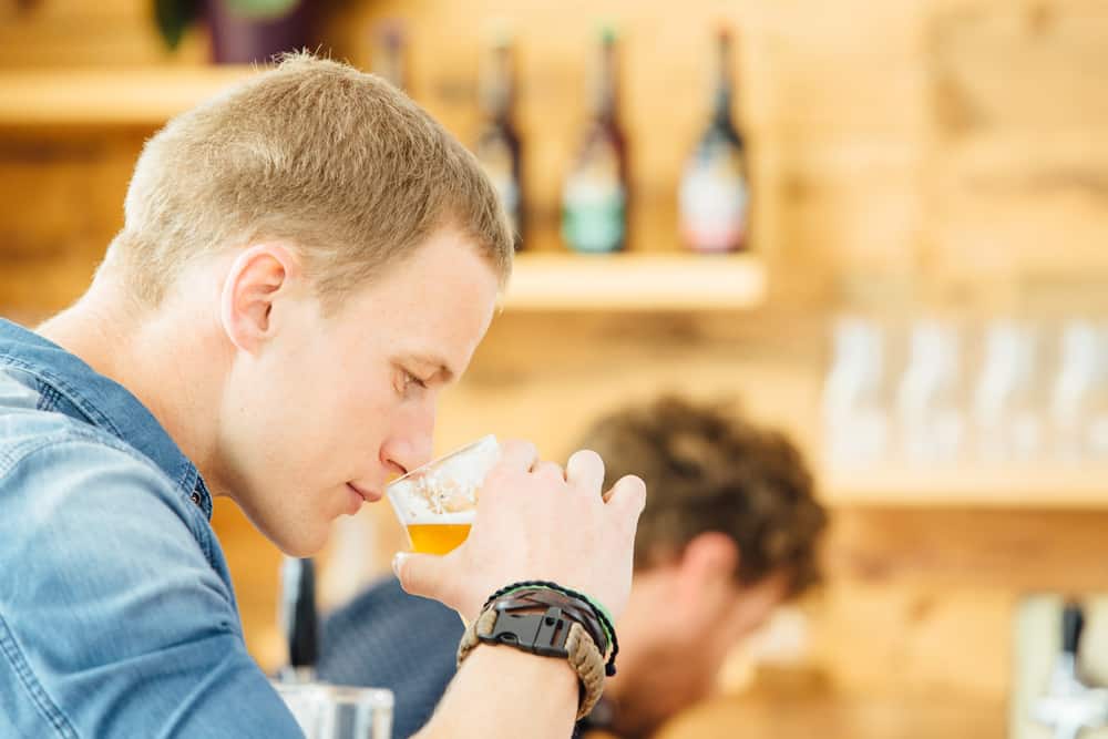 Ung mandlig ølsmager som dufter til et glas med øl.
