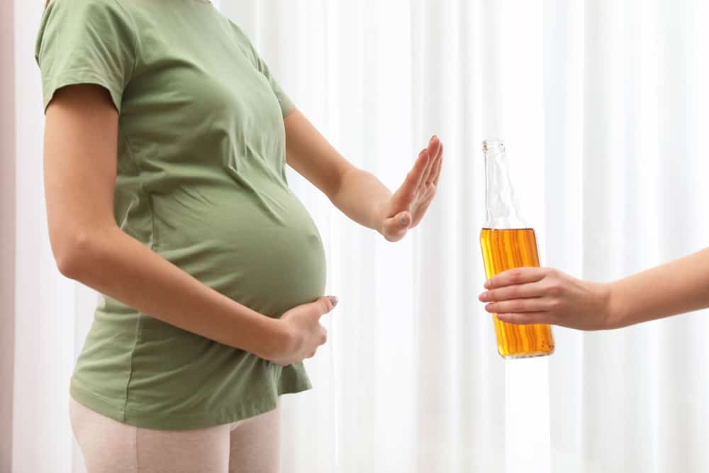 Kvinde holder med sin ene hånd om sin gravide mave, men hun med den anden hånd signalerer "nej tak" til en flaske med øl.