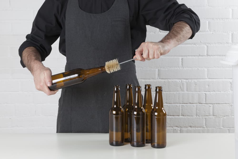 Mand med forklæde der renser tomme ølflasker til hjemmebrygning af øl.