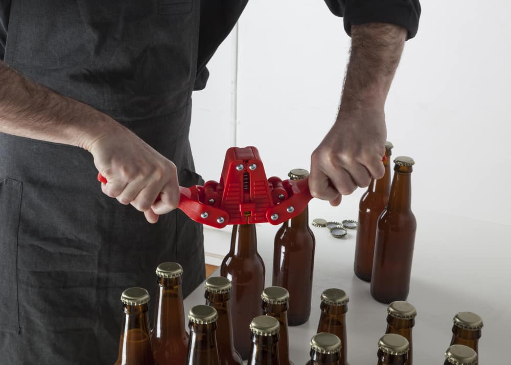 Mand der med håndholdt apparat påsætter kapsler til flasker med hjemmebrygget øl.