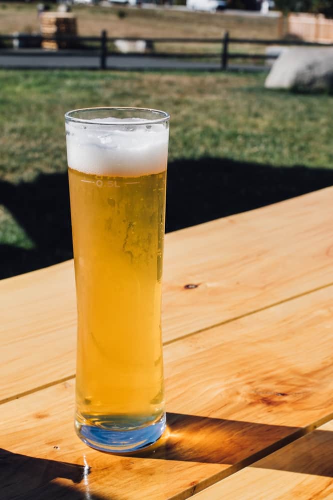 Fyldt Stange ølglas på et træbord med græsplæne i baggrunden.